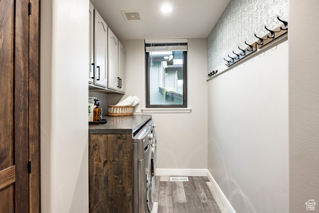 Washroom featuring washing machine and dryer, cabinet space, dark wood finished floors, and baseboards