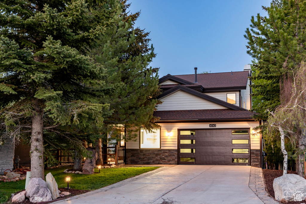 View of front of home with concrete driveway, an attached garage, roof with shingles, and stone siding