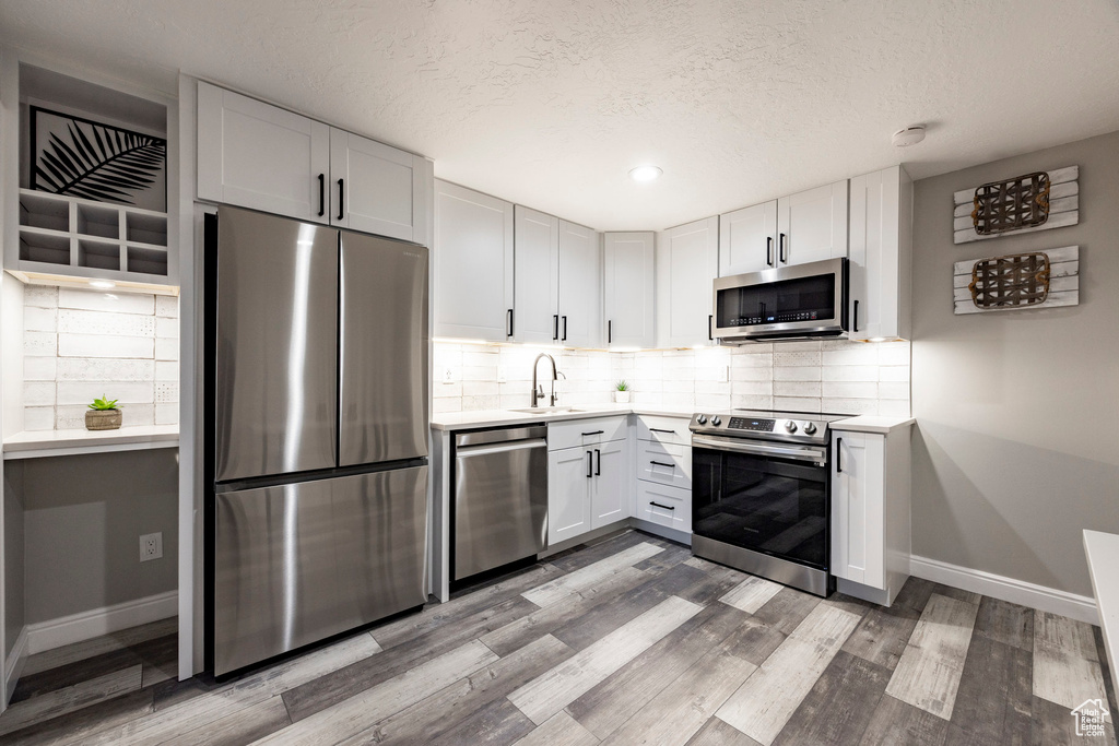 Kitchen with stainless steel appliances, a sink, baseboards, light wood-style floors, and light countertops