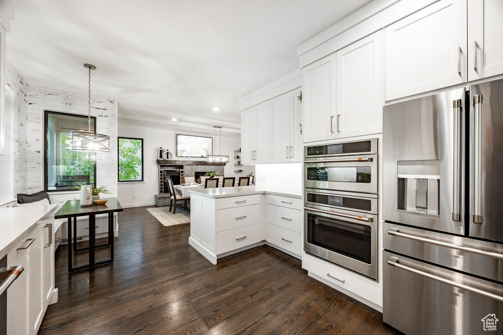 Kitchen with stainless steel appliances, a peninsula, light countertops, white cabinetry, and dark wood finished floors