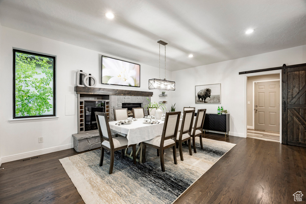 Dining space featuring a barn door, a stone fireplace, baseboards, dark wood-style flooring, and recessed lighting