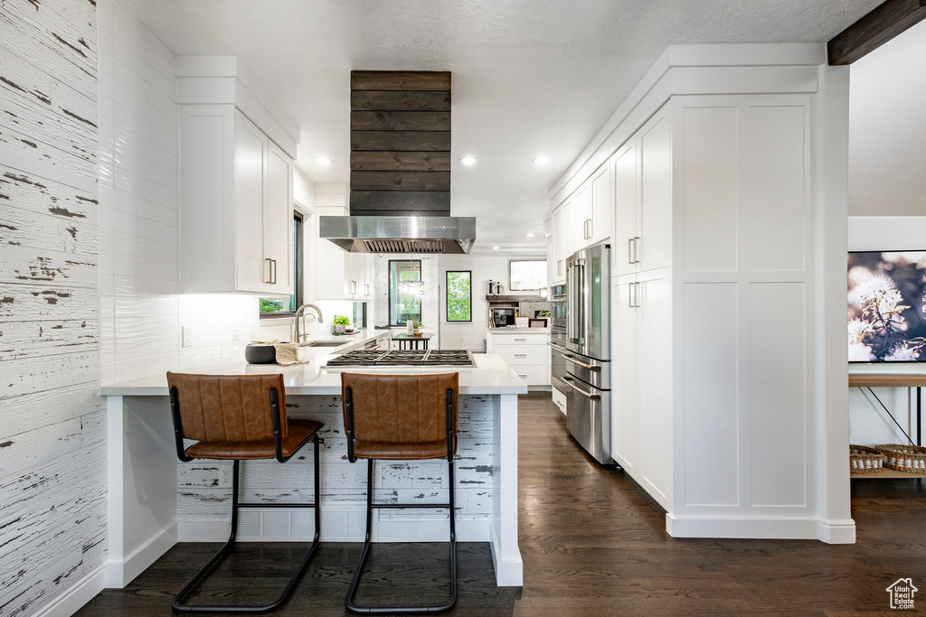 Kitchen with stainless steel appliances, exhaust hood, a peninsula, white cabinets, and recessed lighting