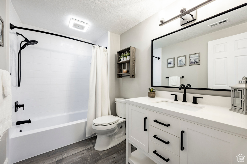 Full bathroom featuring wood finished floors, toilet, shower / bath combo with shower curtain, vanity, and a textured ceiling