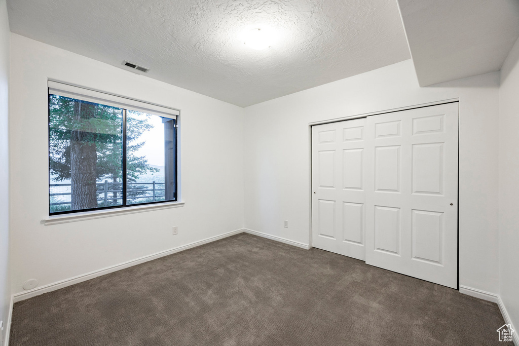 Unfurnished bedroom with dark colored carpet, a textured ceiling, a closet, and baseboards