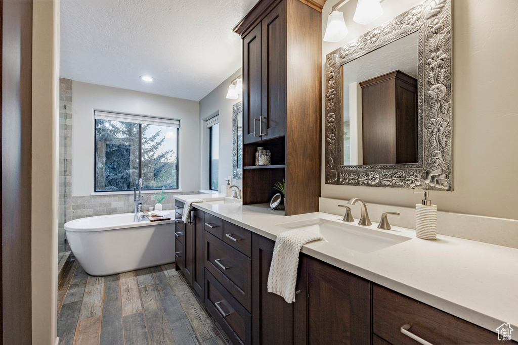 Full bath featuring wood finished floors, a soaking tub, and double vanity