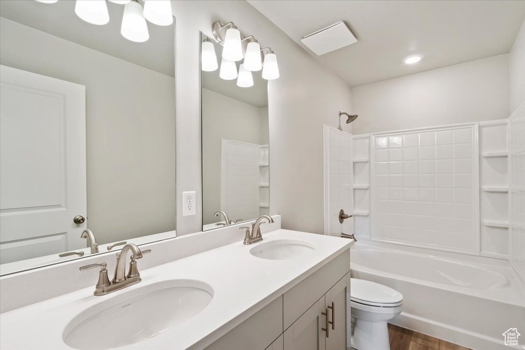 Bathroom with toilet, shower / tub combination, double vanity, and wood finished floors