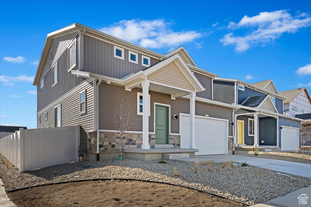 View of front of property featuring a garage, driveway, stone siding, and covered porch