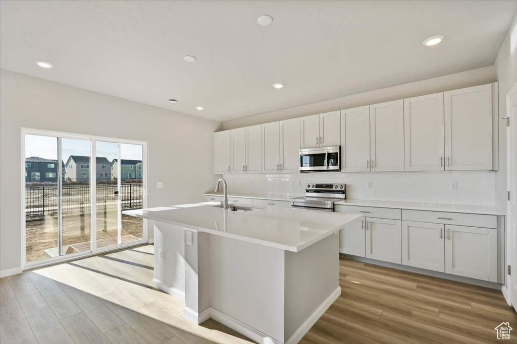 Kitchen with appliances with stainless steel finishes, a sink, light wood-type flooring, tasteful backsplash, and recessed lighting