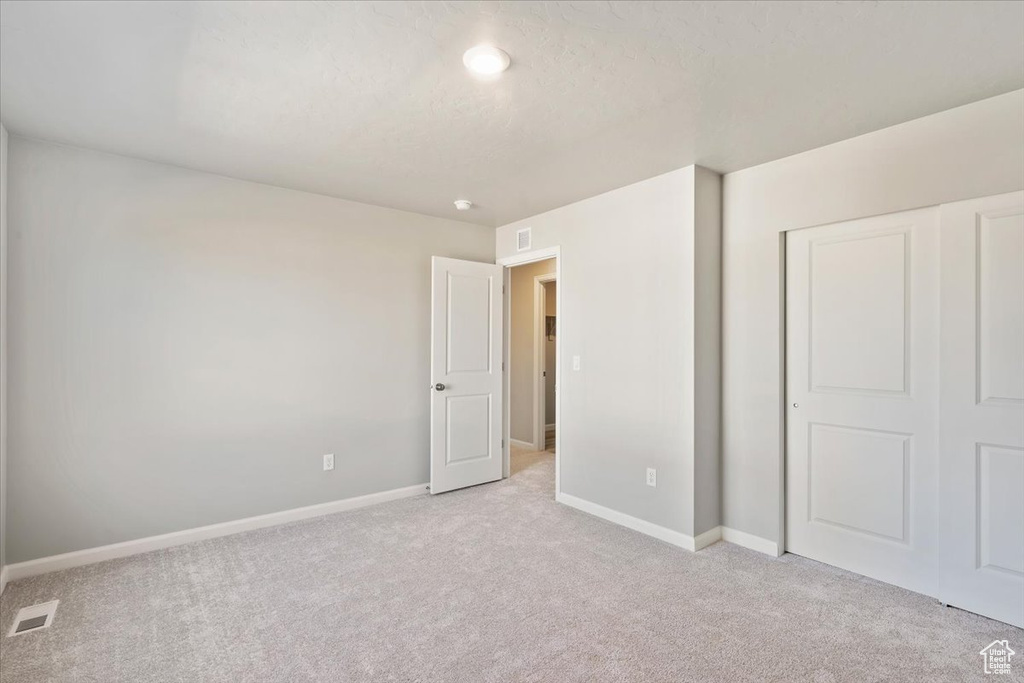 Unfurnished bedroom with light carpet, baseboards, and a closet