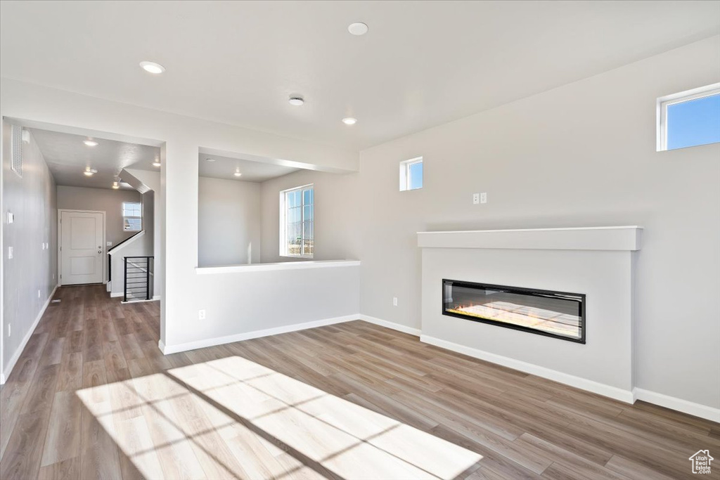 Unfurnished living room with wood finished floors, a glass covered fireplace, baseboards, and recessed lighting