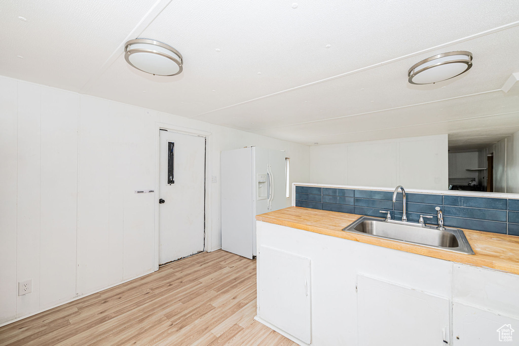 Kitchen with butcher block countertops, white fridge with ice dispenser, a sink, light wood-style flooring, and decorative backsplash
