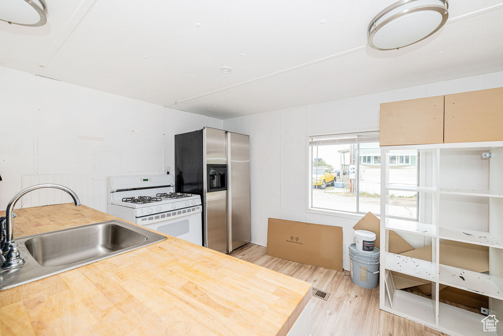 Kitchen featuring white gas stove, stainless steel refrigerator with ice dispenser, a sink, light wood-type flooring, and butcher block counters