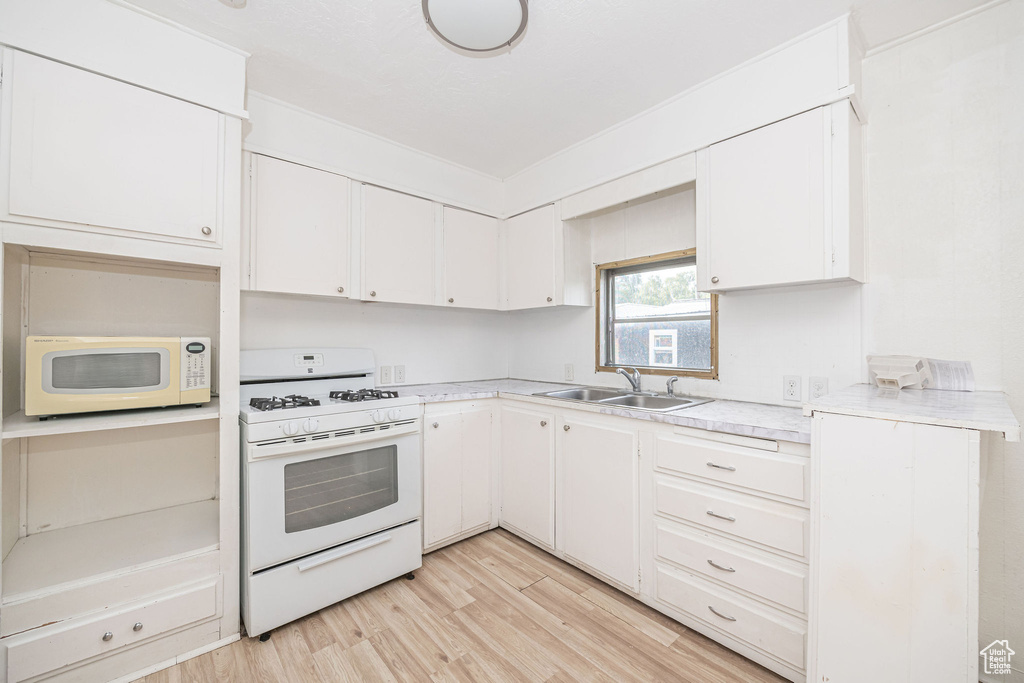 Kitchen featuring white appliances, a sink, light countertops, and white cabinetry