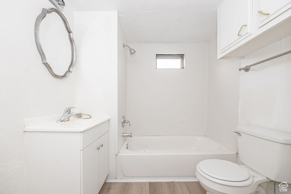 Bathroom featuring toilet,  shower combination, wood finished floors, and vanity