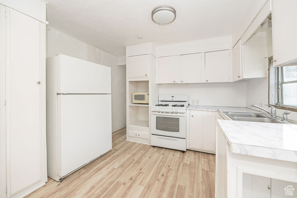 Kitchen featuring white appliances, a sink, light wood finished floors, light countertops, and white cabinetry
