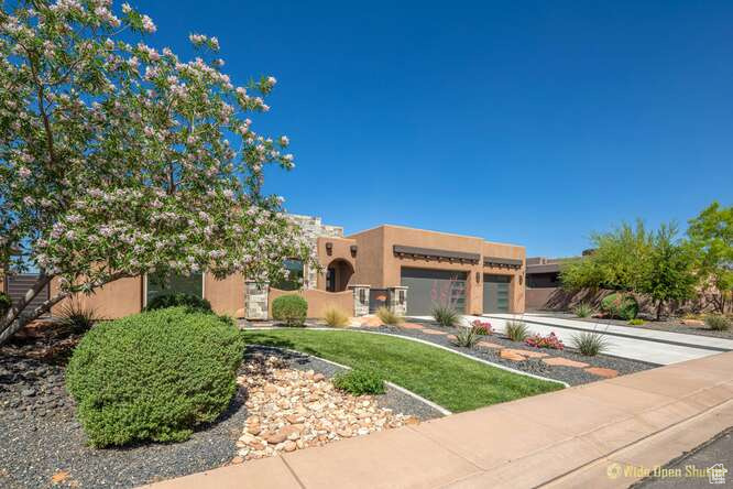 Pueblo-style house with stucco siding, an attached garage, and a front yard