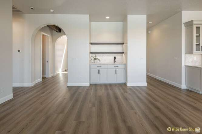 Unfurnished living room featuring arched walkways, wood finished floors, baseboards, and recessed lighting