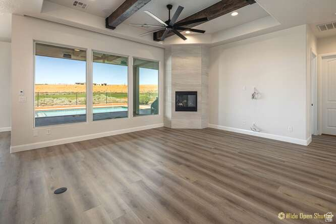 Unfurnished living room with a ceiling fan, wood finished floors, baseboards, beam ceiling, and a fireplace