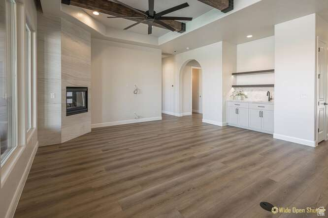 Unfurnished living room featuring arched walkways, a ceiling fan, a premium fireplace, dark wood-type flooring, and beamed ceiling