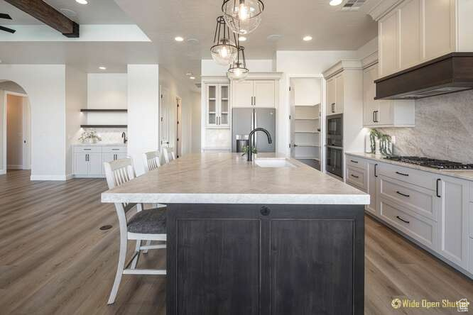 Kitchen featuring arched walkways, gas stovetop, stainless steel fridge with ice dispenser, wood finished floors, and recessed lighting