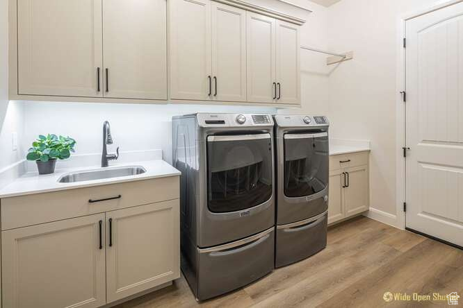 Laundry room featuring separate washer and dryer, light wood-style floors, cabinet space, and baseboards