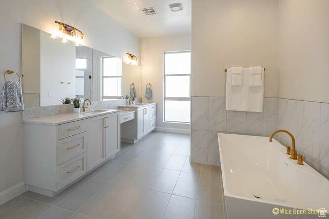 Full bath with a soaking tub, vanity, tile patterned floors, tile walls, and wainscoting
