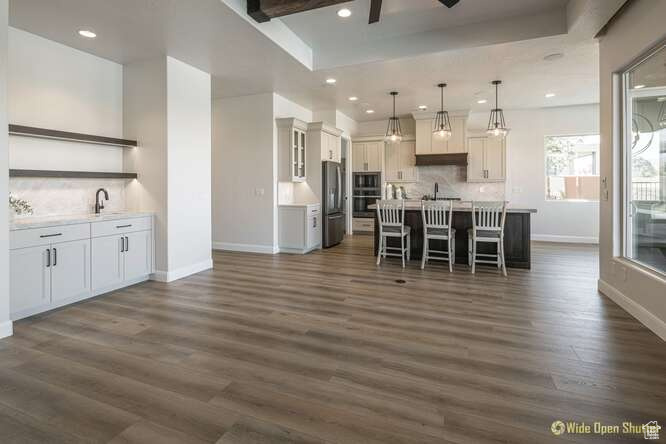 Kitchen featuring open shelves, baseboards, stainless steel appliances, a breakfast bar area, and dark wood-style flooring