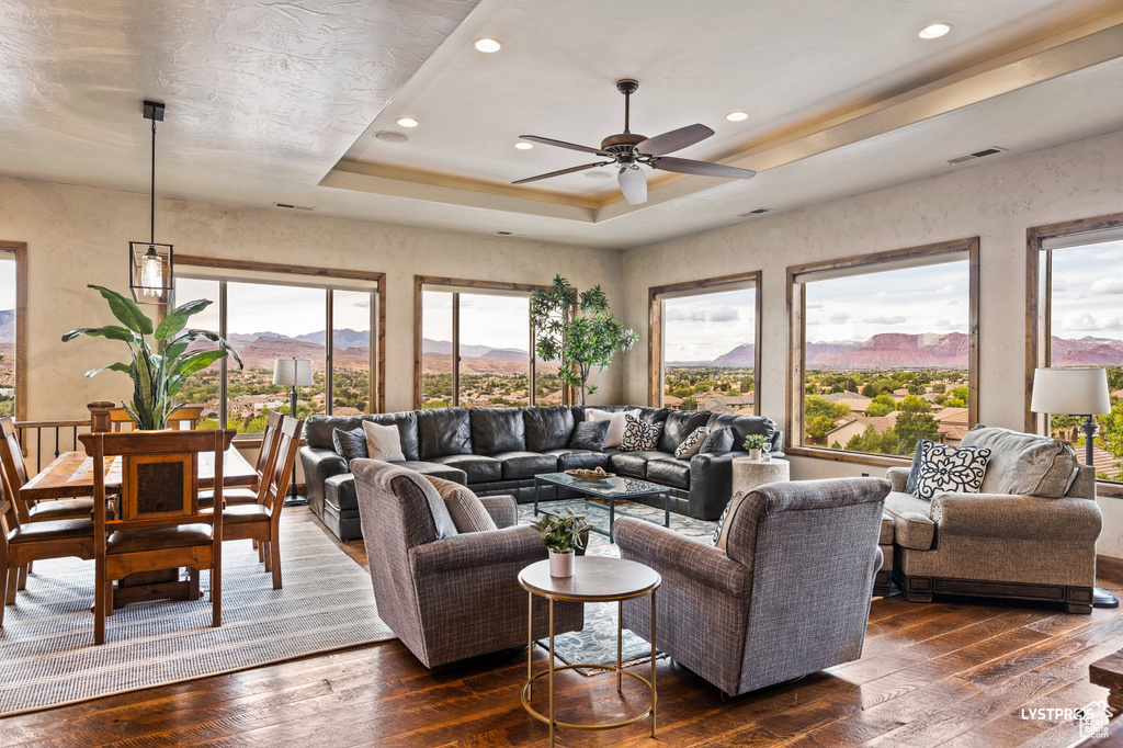 Living room featuring dark wood-style flooring, a mountain view, a ceiling fan, a tray ceiling, and recessed lighting