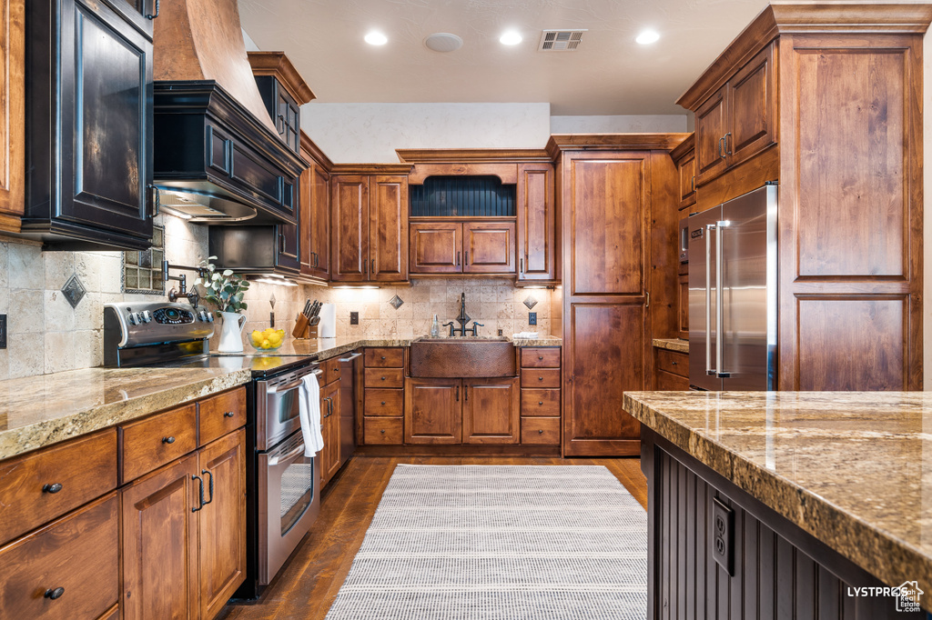 Kitchen featuring stainless steel appliances, a sink, dark wood-type flooring, light stone countertops, and recessed lighting