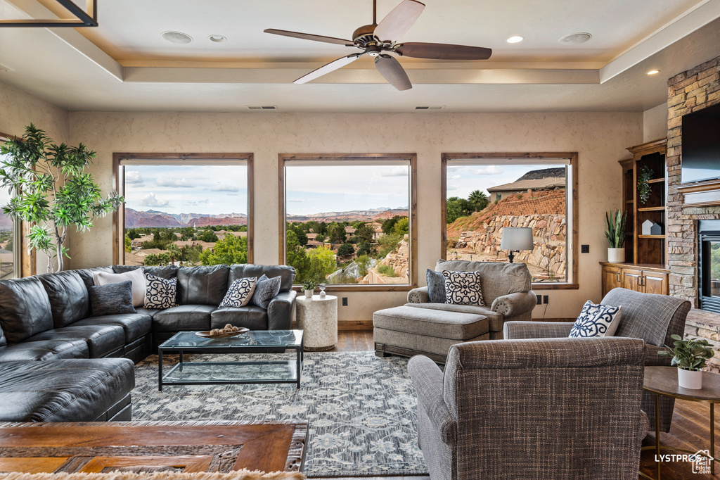 Living area with a tray ceiling, ceiling fan, wood finished floors, recessed lighting, and a fireplace