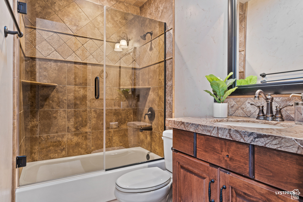 Bathroom featuring toilet, bath / shower combo with glass door, and vanity