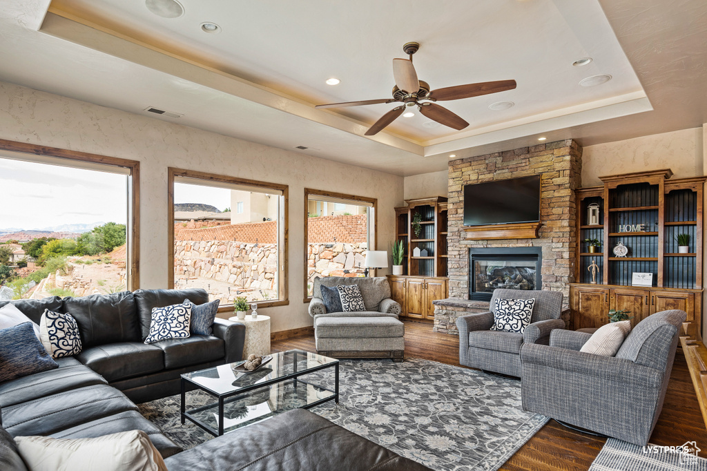 Living room featuring a tray ceiling, a ceiling fan, wood finished floors, a fireplace, and recessed lighting