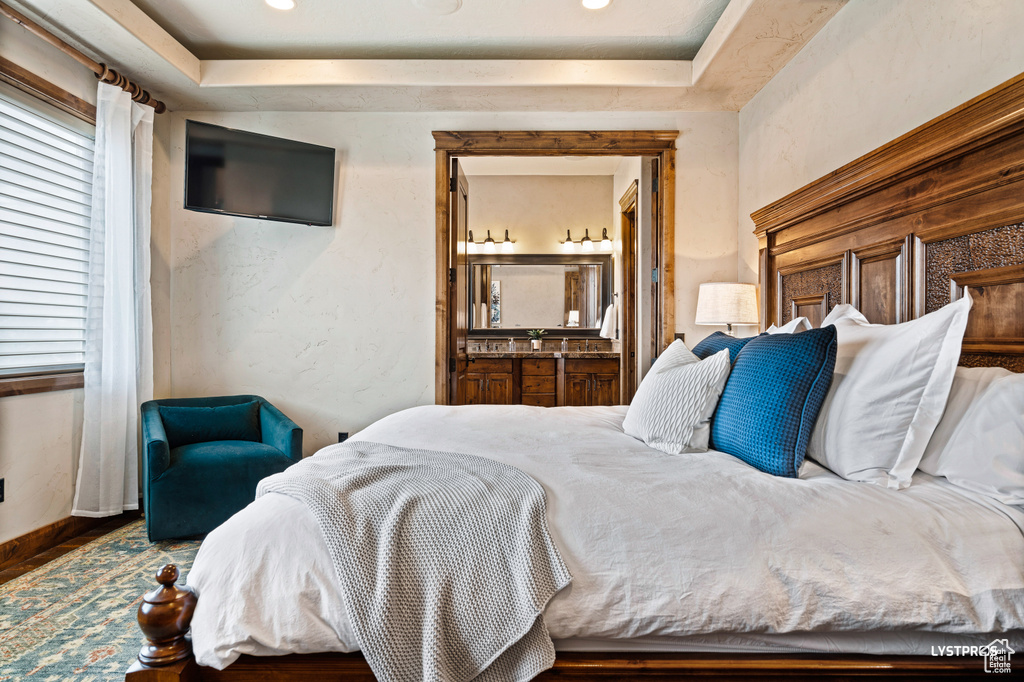 Bedroom featuring a raised ceiling, connected bathroom, wood finished floors, recessed lighting, and baseboards