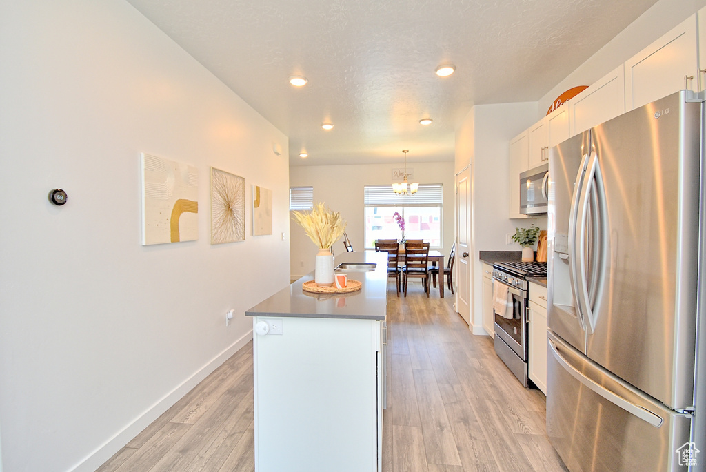 Kitchen with stainless steel appliances, a kitchen island, recessed lighting, white cabinetry, and light wood finished floors