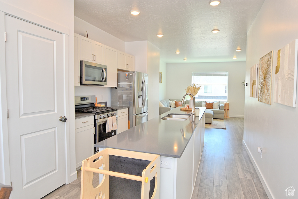 Kitchen featuring appliances with stainless steel finishes, a sink, open floor plan, an island with sink, and light wood-style floors