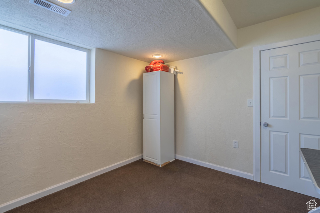 Empty room with dark colored carpet, baseboards, and a textured ceiling