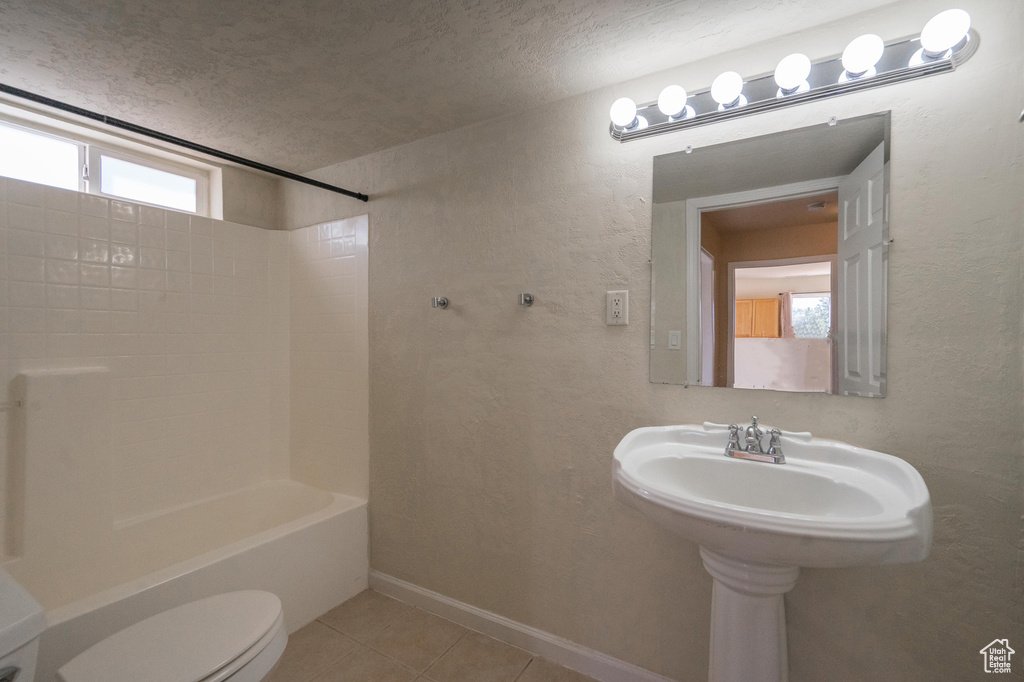Full bath featuring plenty of natural light, tile patterned floors, a textured ceiling, toilet, and washtub / shower combination