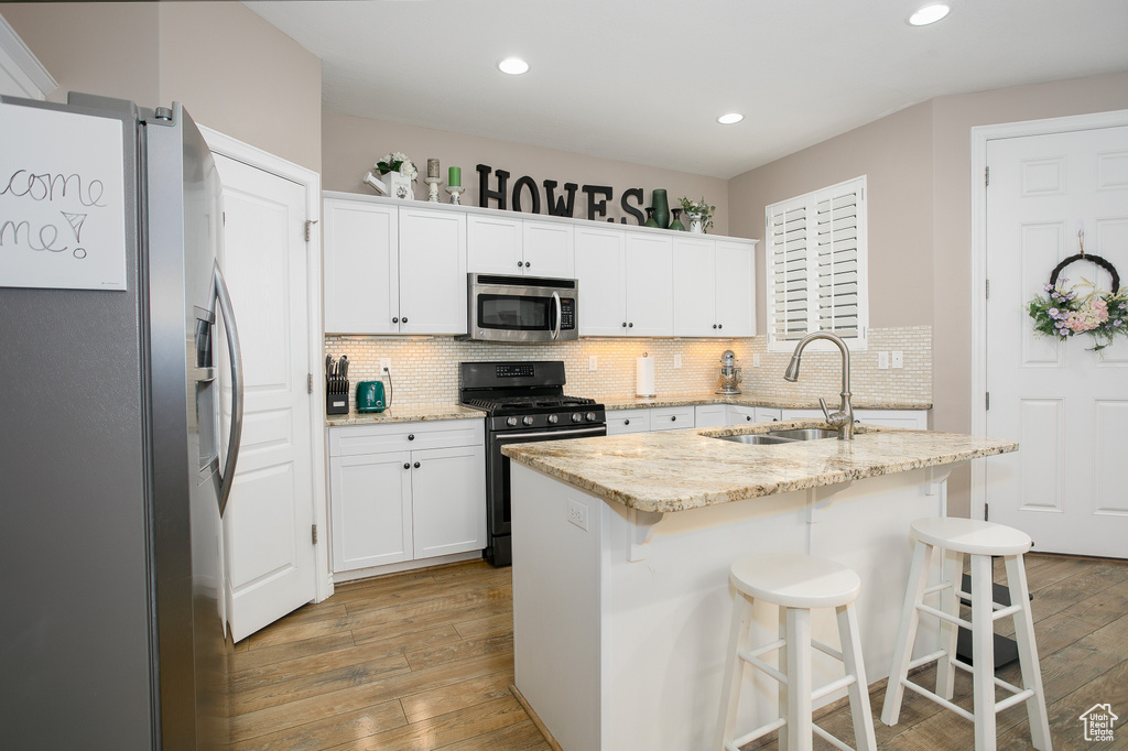 Kitchen with appliances with stainless steel finishes, a sink, light wood finished floors, tasteful backsplash, and recessed lighting