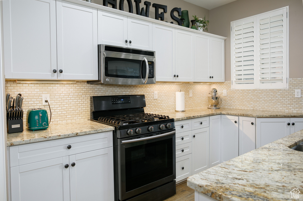 Kitchen with appliances with stainless steel finishes, white cabinetry, light stone counters, and decorative backsplash