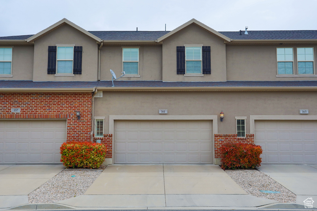 Multi unit property featuring a garage, brick siding, stucco siding, and driveway