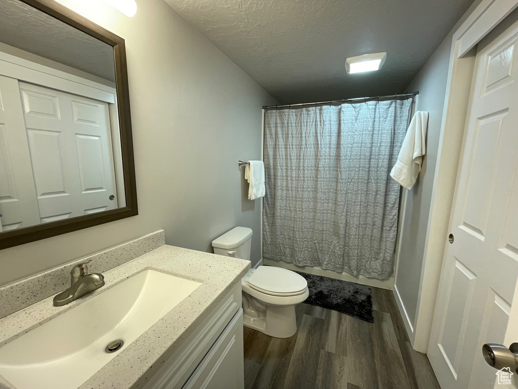 Full bathroom featuring wood finished floors, toilet, vanity, a textured ceiling, and curtained shower
