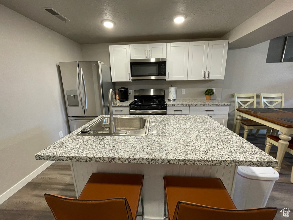 Kitchen featuring appliances with stainless steel finishes, a sink, white cabinets, baseboards, and dark wood-type flooring