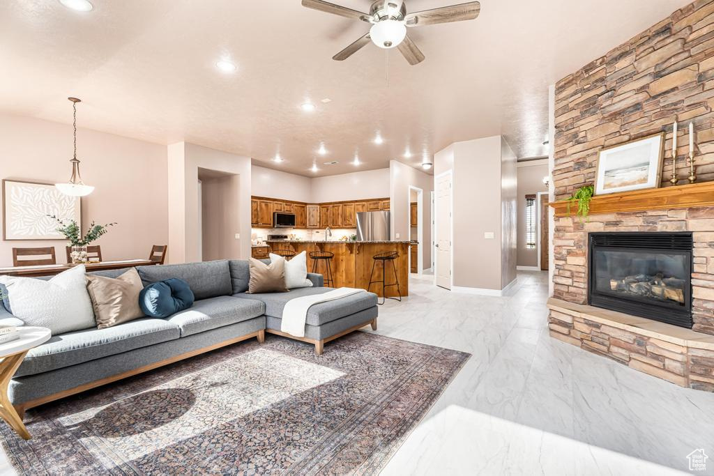 Living area with a ceiling fan, recessed lighting, light marble finish flooring, and a fireplace