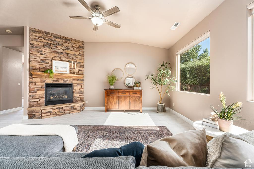 Living room featuring a ceiling fan, vaulted ceiling, a stone fireplace, and baseboards