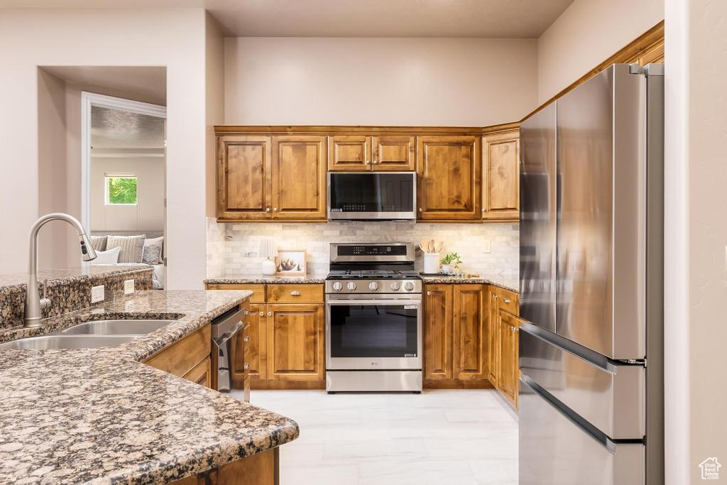 Kitchen with stainless steel appliances, a sink, brown cabinets, decorative backsplash, and stone counters