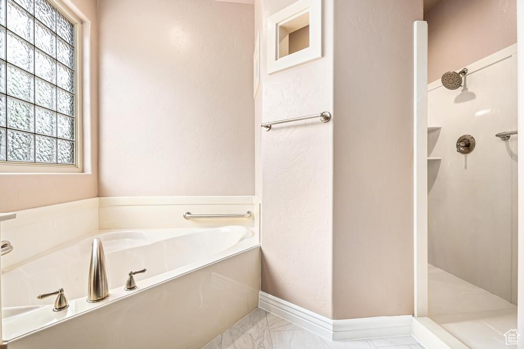 Bathroom featuring marble look tiles, a walk in shower, a bath, and baseboards