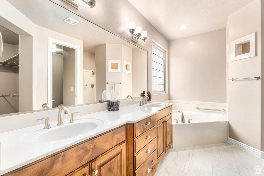 Full bathroom featuring a bath, double vanity, marble finish flooring, baseboards, and a walk in closet