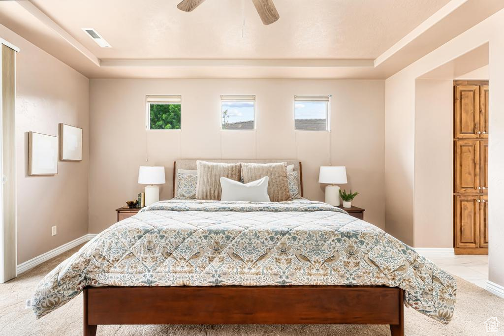 Bedroom with a raised ceiling, light colored carpet, baseboards, and ceiling fan