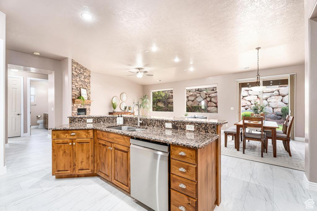 Kitchen featuring a sink, dishwasher, light marble finish flooring, ceiling fan, and brown cabinetry