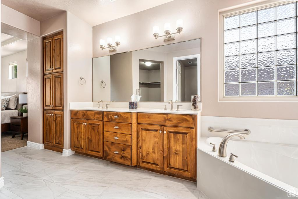 Bathroom with marble look tiles, a bath, and double vanity